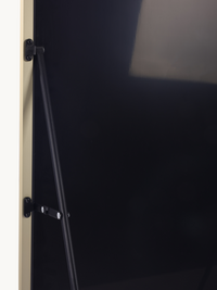 Close-up of black metal support rod and two mounting brackets fixed to the gold aluminium frame edge of a standing mirror