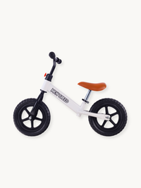 White New Speed balance bike side view, white steel frame with brand logo, tan saddle, black five-spoke wheels and rubber…