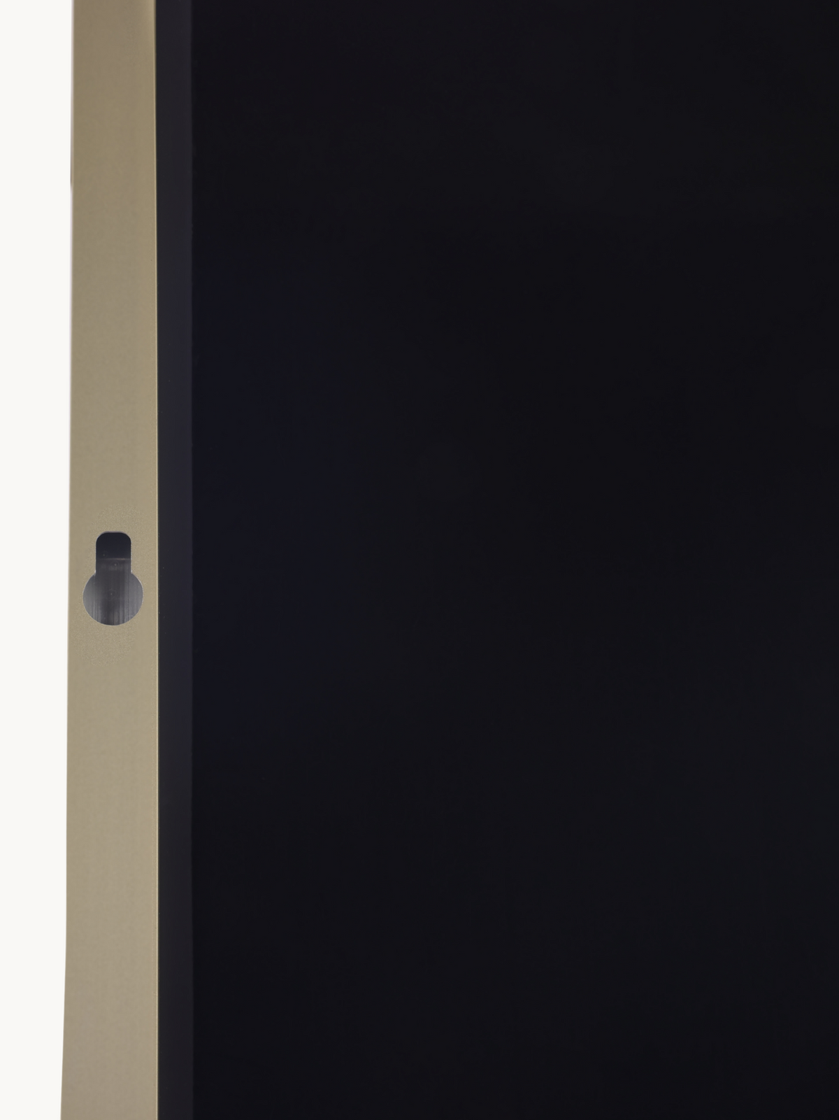 Close-up of gold aluminium frame edge showing a small circular keyhole-shaped wall-mount fitting on a black mirror panel