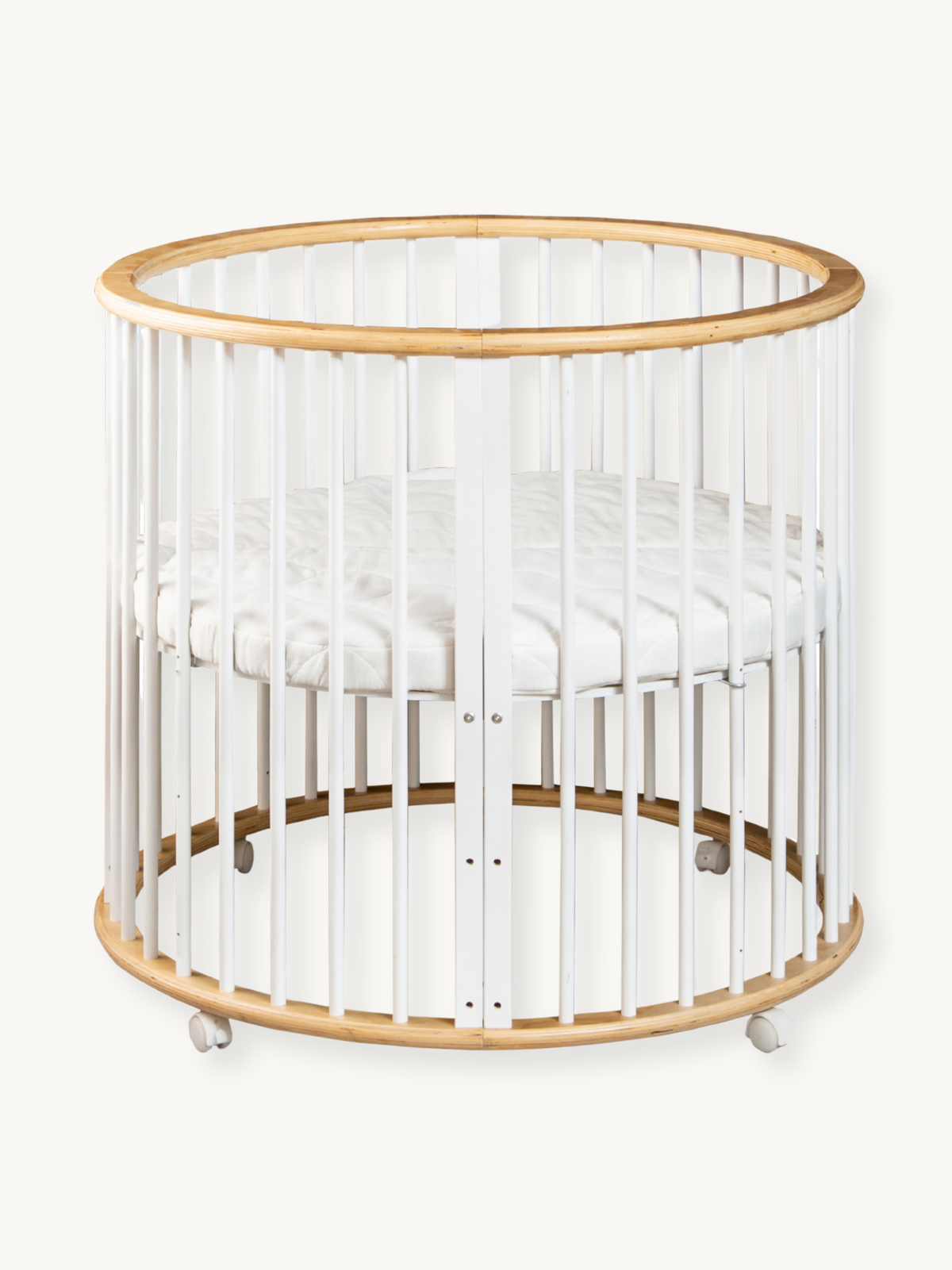Round wooden baby playpen with white vertical slats, natural wood top and base rings, white mattress inside, on castors, f…