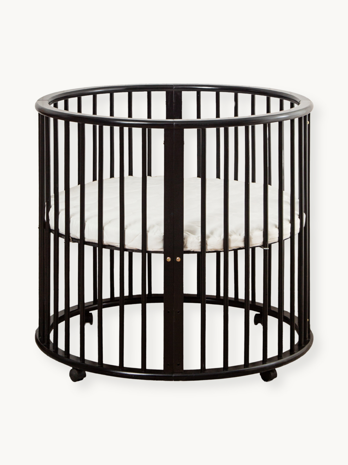 Black round wooden playpen Sami with vertical slats, curved top rail, small caster feet, and white fitted oval mattress in…