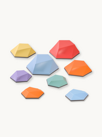 Eight multicolour hexagonal balance stones in three sizes, scattered on white background, with faceted tops and dark non-s…