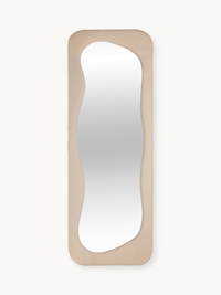 Tall rectangular mirror with wavy organic-shaped glass set in a cream white teddy fabric upholstered frame, front view on…