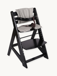 Black wooden adjustable highchair with light grey cushion insert and brown safety harness, angled front view on white back…