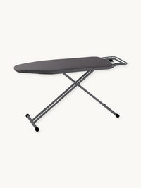 Dark grey ironing board with cotton cover, iron rest at narrow end, cross-frame steel legs and rubber feet, angled side view