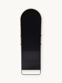 Rear view of tall arched standing mirror showing black panel back, gold aluminium frame edge, and black metal base bar