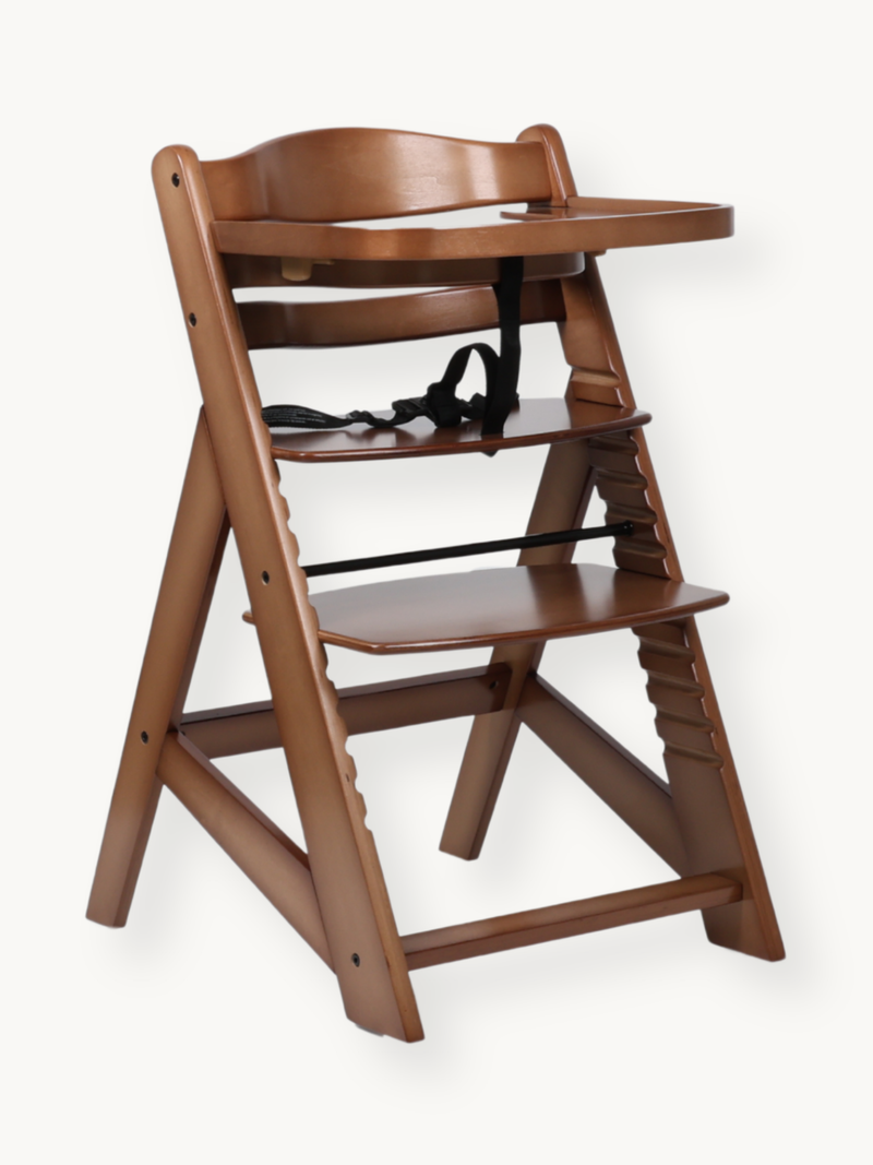 Walnut-stained solid wood adjustable baby high chair with black safety harness and attached tray, angled front view