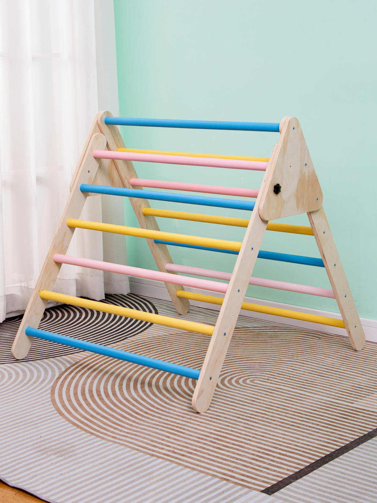 Wooden Pikler triangle climbing frame with pastel rungs in a mint-green children's room, placed on a patterned play rug
