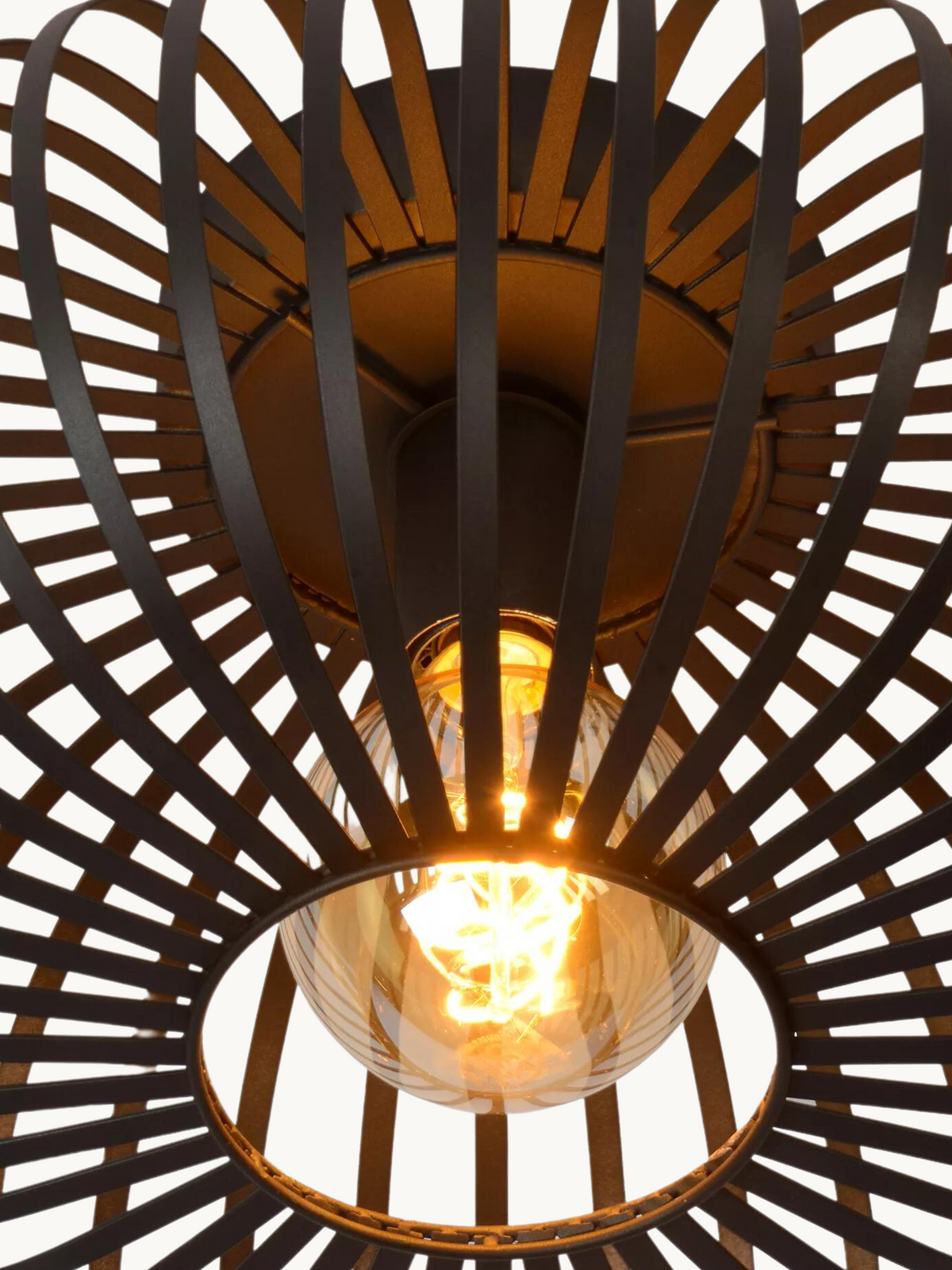 Close-up shot looking up into black metal cage shade, lit spiral filament bulb glowing amber at centre, crossed strap weav…