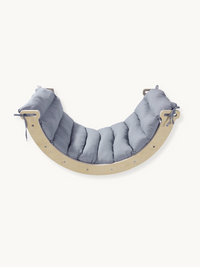 Curved wooden climbing arch rocker with quilted grey tie-on cushion, front view on white background
