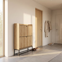 Oak-finish Japandi shoe cabinet in a hallway, front-facing, with ribbed doors and black metal legs, shoes stored underneath
