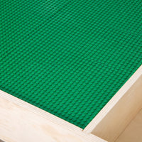 Close-up of green building plate surface fitted into natural wood table frame, showing stud texture and panel join line