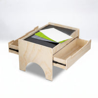 Natural wood play table angled from below, both side drawers open, showing grey chalkboard surface with green, white and g…