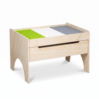 Natural wood children's play table with green, white and grey building plates on top and a sliding storage drawer below, a…