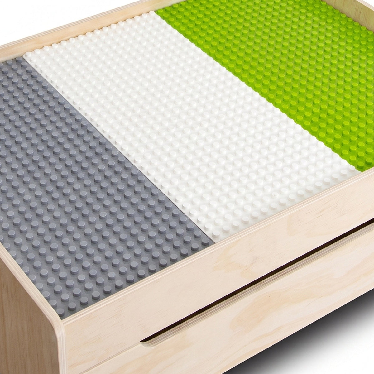 Close-up top-down angle of grey, white, and green building baseplates fitted inside a natural wood play table with drawer…
