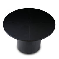 Black round dining table overhead view showing four-panel tabletop seams and fluted cylindrical pedestal base, matte black…