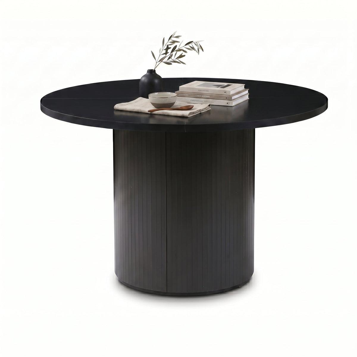 Black round dining table with ribbed pedestal base, styled with a dark vase, stacked books and a ceramic bowl, three-quart…