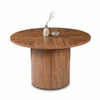 Angled front view of round walnut dining table, herringbone top with small vase and bowl, ribbed cylindrical pedestal base…