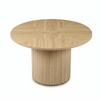 Angled top-down view of round oak dining table showing radiating wood-grain segments on tabletop and vertical-slatted cyli…