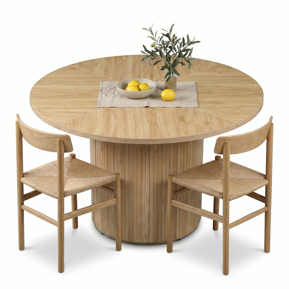 Natural oak round dining table with fluted cylinder base, styled with two woven-seat chairs, lemon bowl and olive branch c…