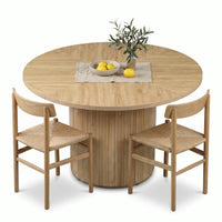 Natural oak round dining table with fluted cylinder base, styled with two woven-seat chairs, lemon bowl and olive branch c…