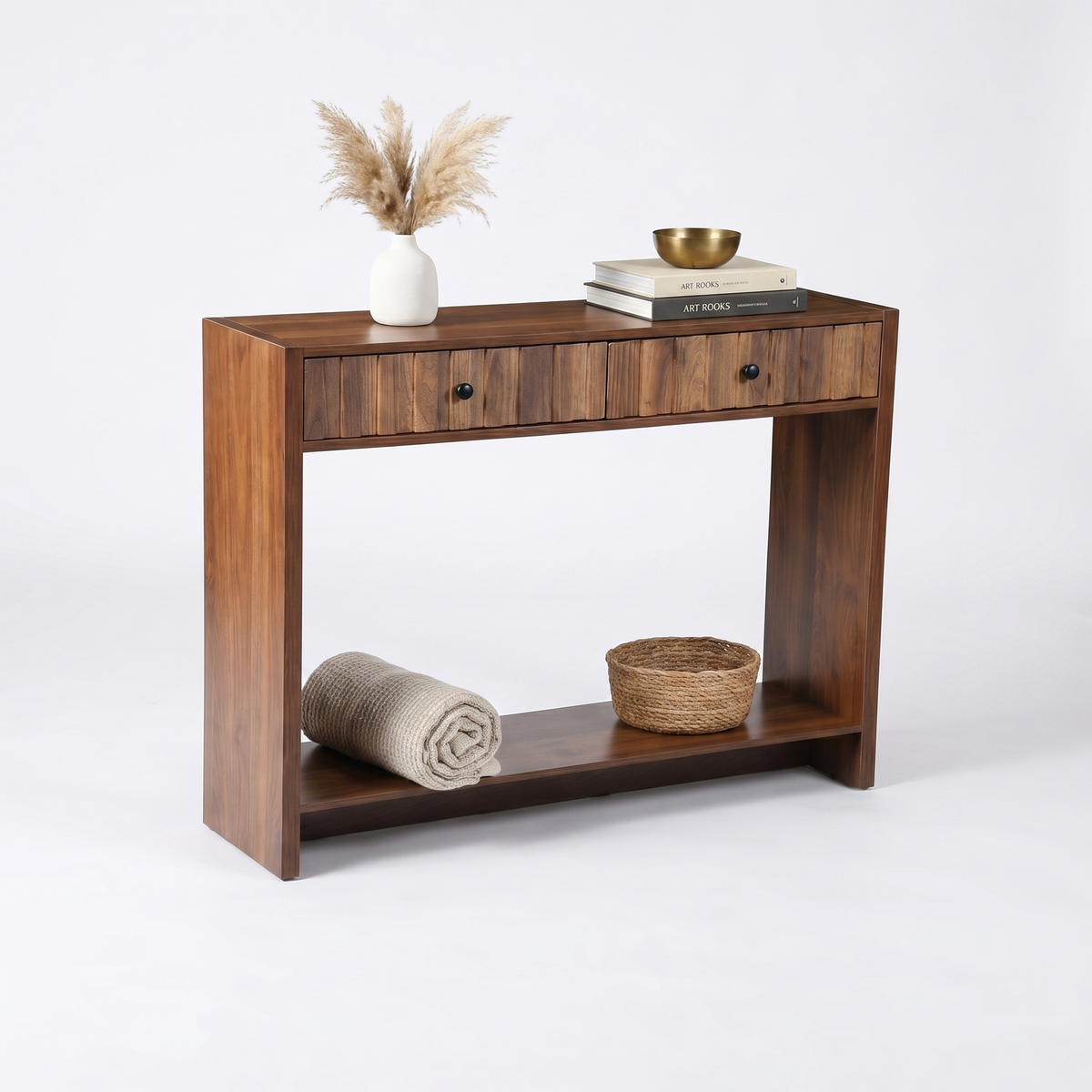 Walnut console table angled view styled with pampas grass, stacked books and gold bowl on top, rolled blanket and wicker b…