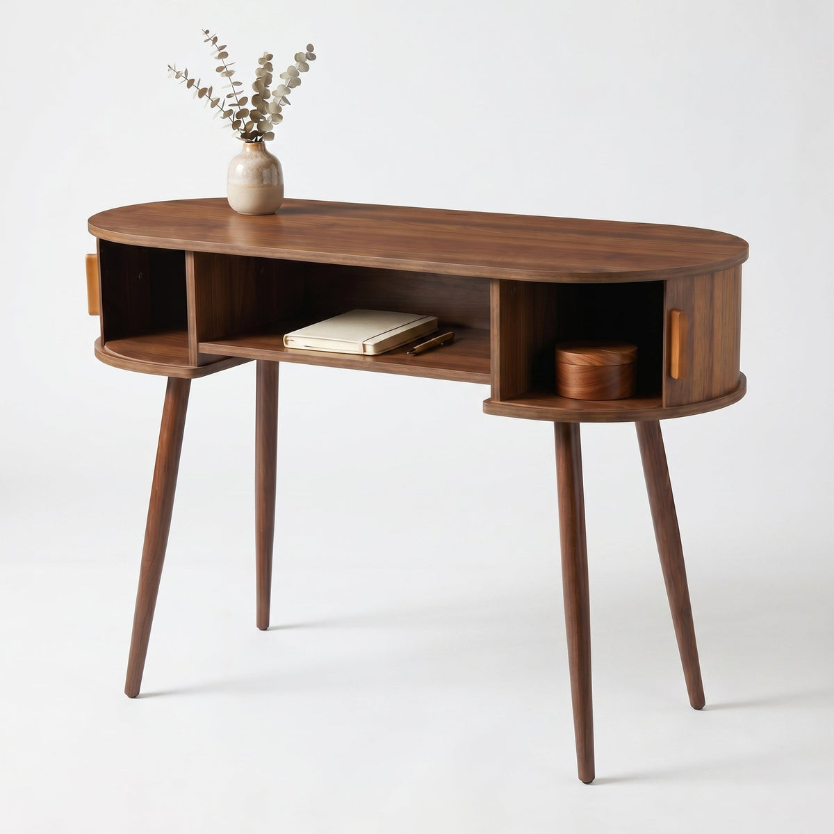 Walnut oval console table angled view, open centre shelf holding a notebook, small wooden box, and ceramic vase with dried…