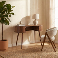 Walnut oval console table styled with a lamp, books, and boucle chair beside sheer curtains and a fiddle-leaf fig plant