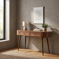 Walnut oval console desk with two recessed drawers, styled in a sunlit room with a table lamp, stacked books and small pot…