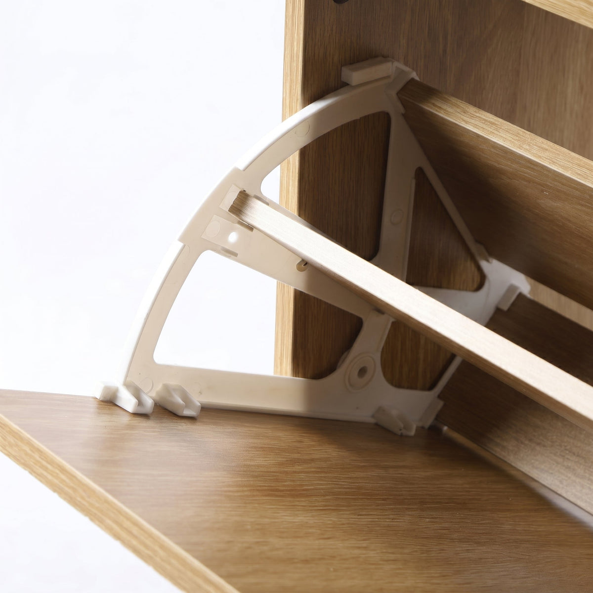 Close-up of white plastic folding hinge bracket connecting oak slat panel to cabinet body, underside angle