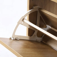 Close-up of white plastic folding hinge bracket connecting oak slat panel to cabinet body, underside angle