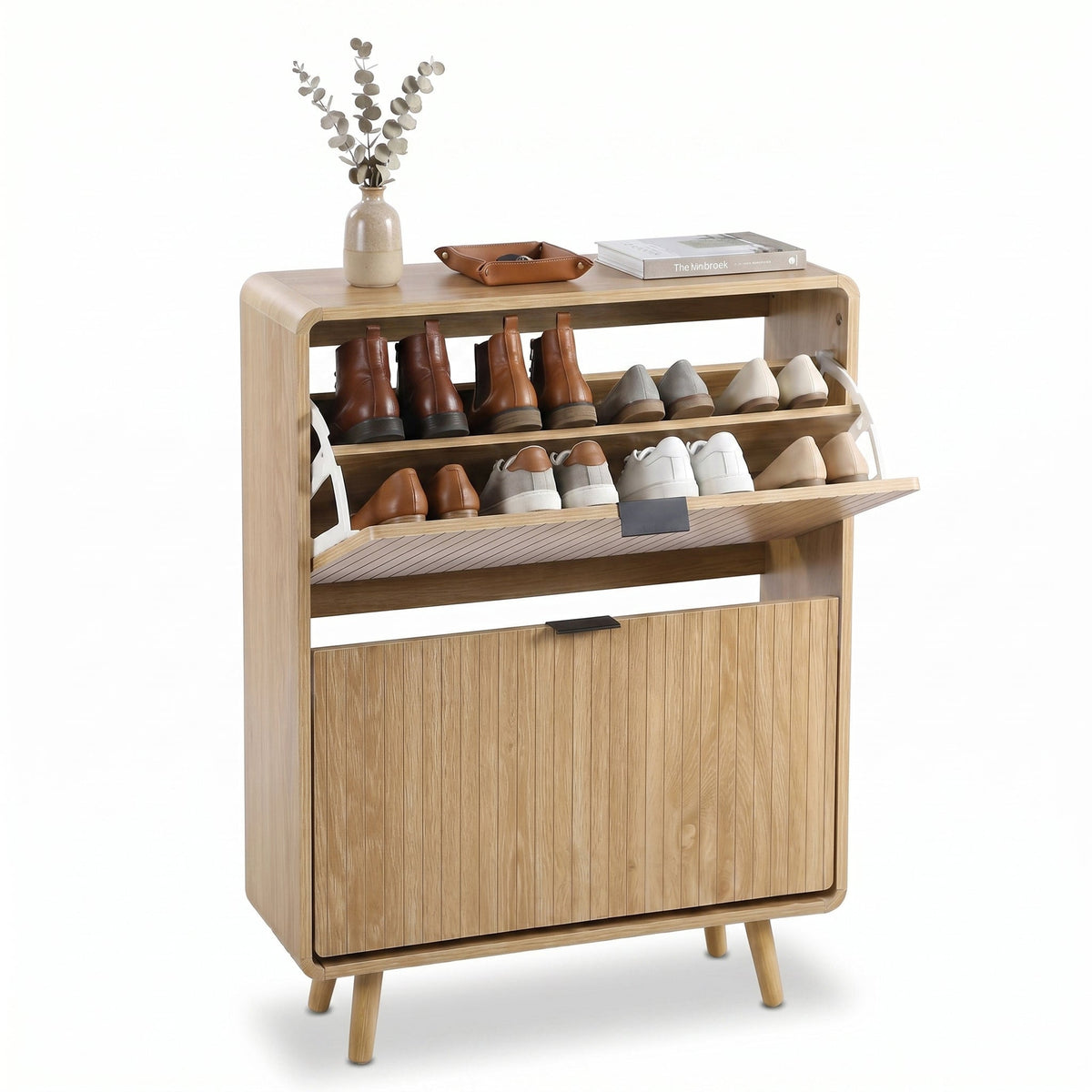 Light oak shoe cabinet open showing boots and sneakers on upper shelves, lower flip-down door closed, topped with vase and…