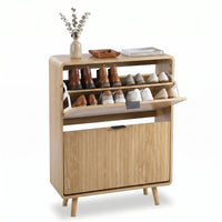 Light oak shoe cabinet open showing boots and sneakers on upper shelves, lower flip-down door closed, topped with vase and…