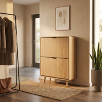Light oak shoe cabinet styled in a hallway with coat rack, jute rug, and snake plant; angled front view showing slatted do…