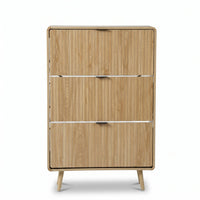 Angled front view of tall light oak shoe cabinet showing vertical wood grain, three flush flip-down doors with slim black…