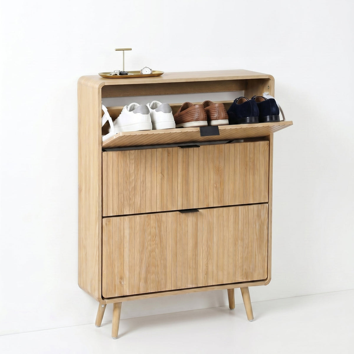 Light oak shoe cabinet with top flip-door open, revealing three pairs of shoes; two closed flip drawers below; splayed leg…