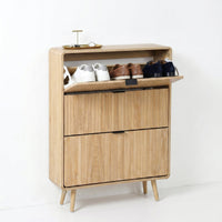 Light oak shoe cabinet with top flip-door open, revealing three pairs of shoes; two closed flip drawers below; splayed leg…