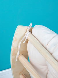 Close-up of cream cushion fabric tie knotted around a pine rung on the underside of the climbing arch rocker, teal background