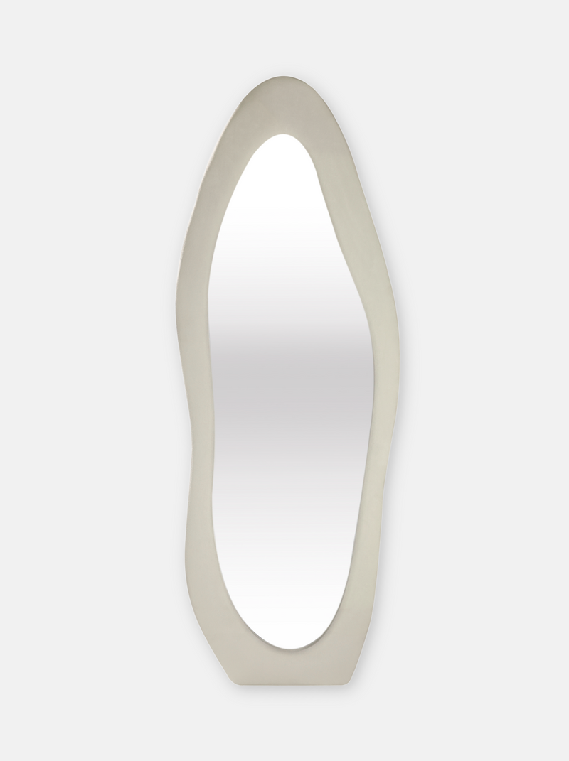 Tall asymmetric standing mirror with white suede velvet upholstered frame, wavy organic silhouette, front view on light gr…