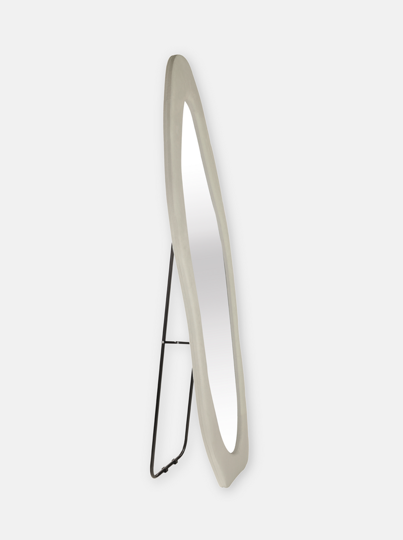 Angled side view of full-length standing mirror with white suede velvet asymmetric frame and black metal easel back stand