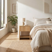 Light oak Japandi bedside table styled in a sunlit neutral bedroom beside a bed with linen bedding and chunky knit throw