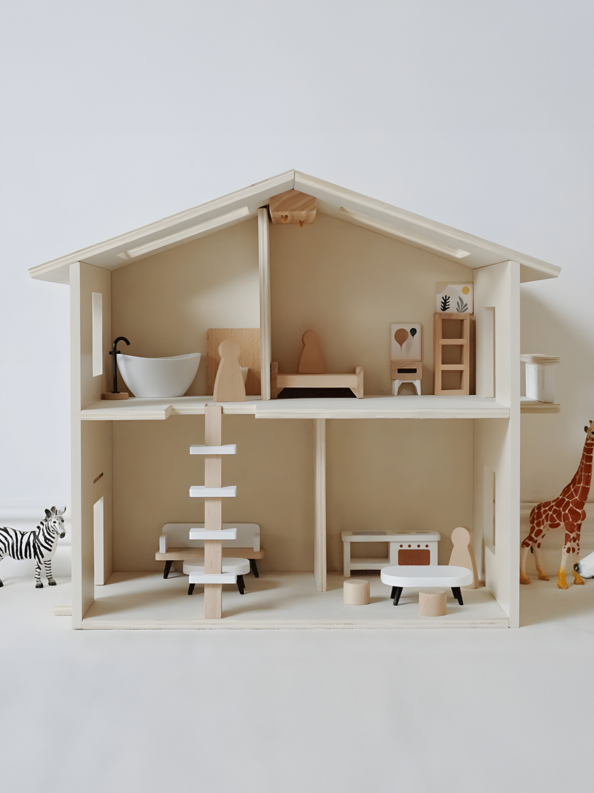 Front-facing natural wood dolls house with miniature bath, bed, kitchen, staircase, and zebra and giraffe figures placed e…