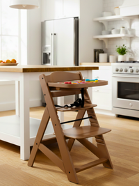 Walnut wood adjustable high chair with colourful toys on tray, styled in bright white kitchen beside island, 3/4 angle