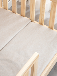 Angled close-up of cream white mattress centre seam inside natural pine crib, showing woven fabric texture and snug fit ag…