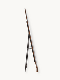 Side profile view of Noa standing mirror showing walnut-finish wood frame edge and black metal easel legs with silver cros…
