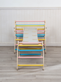 Front view of grey wooden kids climbing set with triangle frame, arch, and ramp connected, showing pink, blue, and yellow…