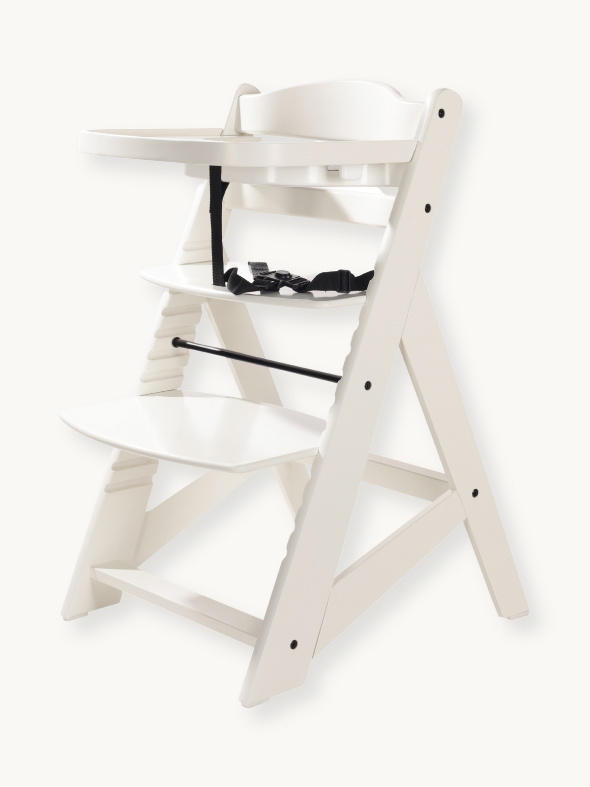 White wooden baby high chair angled view showing adjustable footrest steps, black harness straps with buckle, and attached…