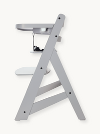 Grey wooden highchair side profile view showing A-frame legs, adjustable footrest, attached tray, and black safety harness…
