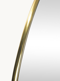 Close-up of brushed matte gold PVC frame edge curving across the upper-left section of the Alaric wall mirror