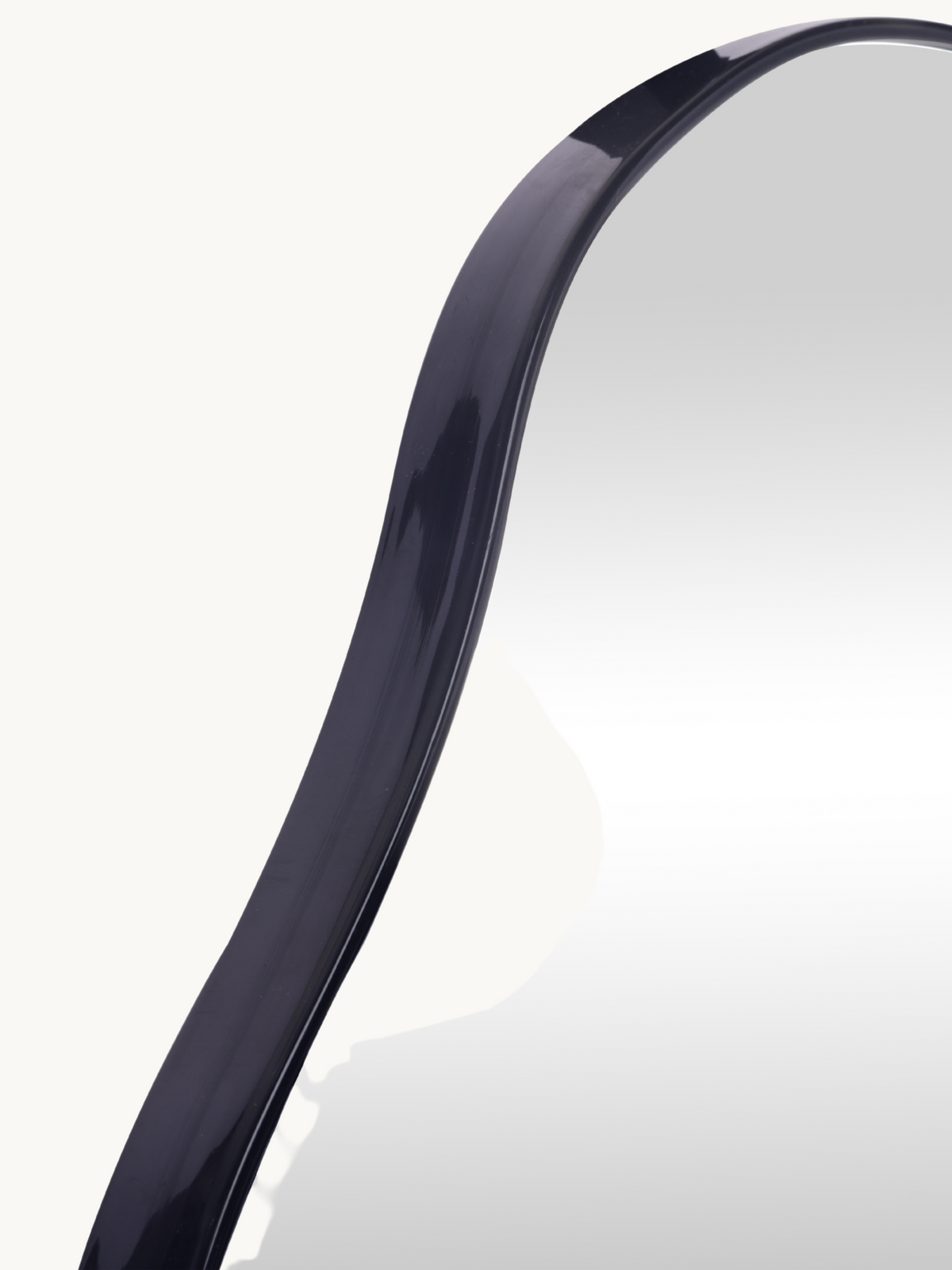 Close-up of upper curve of black gloss PVC frame on organic-shaped Matteo wall mirror, showing frame profile and mirror su…